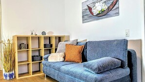 Un salon moderne avec un canapé bleu, un plancher en bois et une bibliothèque agrémentée d’objets décoratifs.