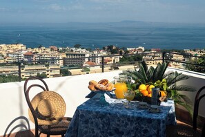 Une table dressée sur un balcon donnant sur un paysage urbain côtier, avec des bâtiments et la mer en toile de fond.