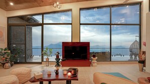 Een ruime woonkamer met grote ramen, een open haard en uitzicht op zee.