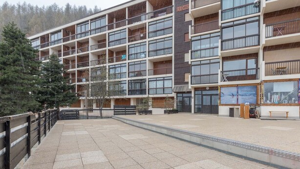 A multi-story hotel with balconies, a ski shop, and a view of a forested area. - Nice studio 4 pers near the slopes (Orcières)