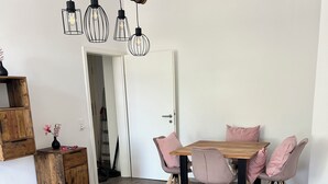 Et spiseområde med et træbord og fire stole, en hængende lysekrone og et træskab med en fletkurv.