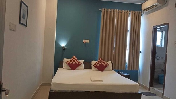 Habitación de hotel con cama, mesita de noche, aire acondicionado de pared y puerta al baño.