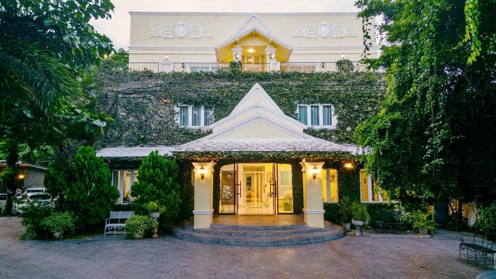 A hotel entrance with a covered porch, steps leading up to the door, and a garden area with benches.