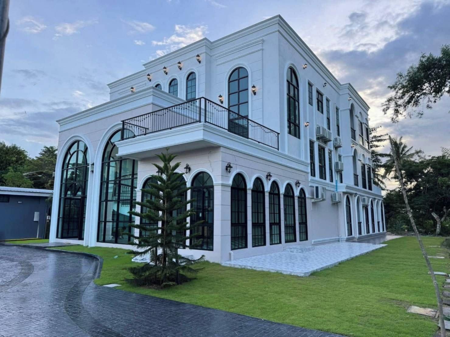 A two-story building with a white exterior, large arched windows, and a balcony with a black railing.