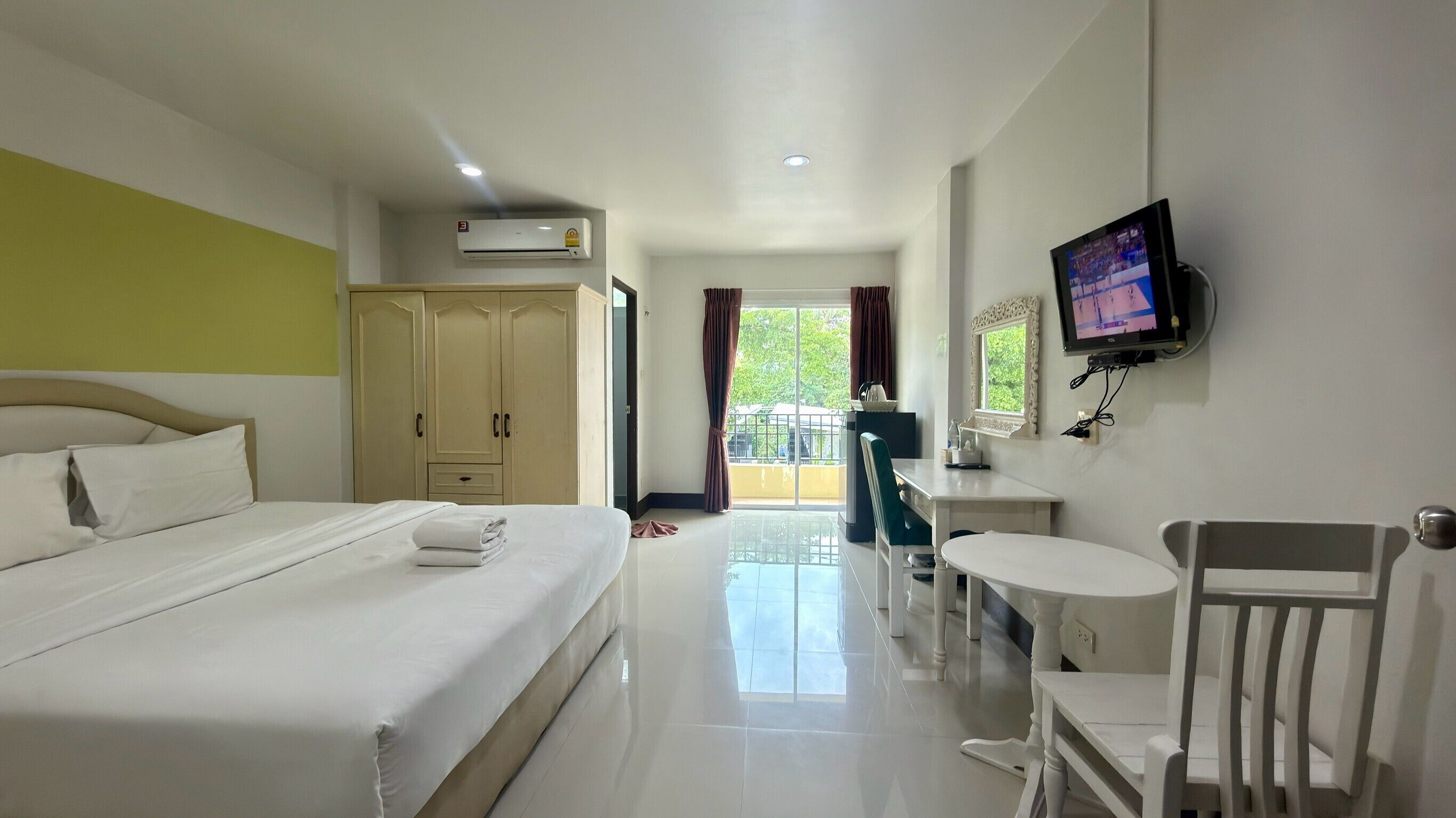 Habitación de hotel con cama, escritorio, silla, televisor y ventana con cortinas.