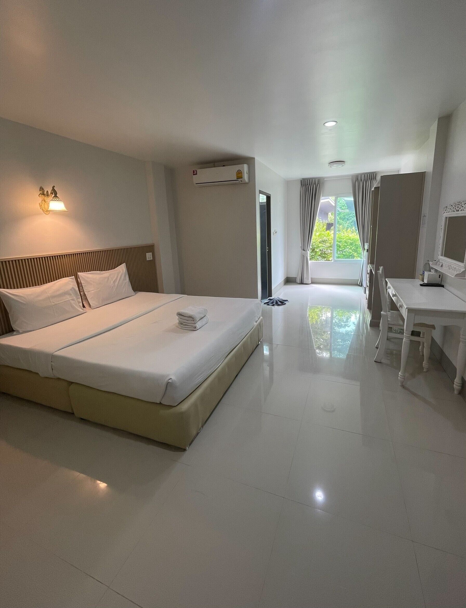 A hotel room with a bed, bedside table, desk, and a view of greenery outside.