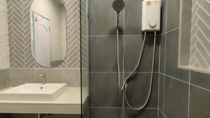 A bathroom with a white sink, a mirror, a shower with a handheld showerhead, and a wall-mounted soap dispenser. - The Target Hotel chaingrai  (Chiang Rai)