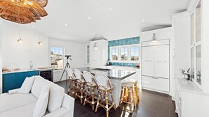 A modern kitchen with a central island, white cabinetry, and a dining area with wicker chairs.