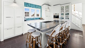A modern kitchen with white cabinetry, a large island with stools, and a view of the outside.
