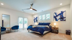 A bedroom with a bed, two chairs, a desk, a ceiling fan, and artwork on the walls. - The Kirkwood Escape!! (Atlanta)