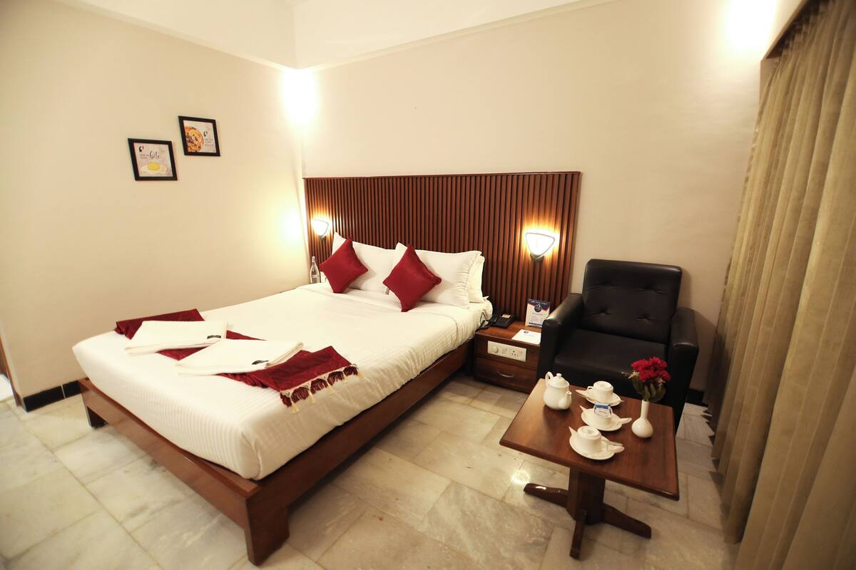 A hotel room with a bed, a chair, a nightstand, and a small table with tea set.
