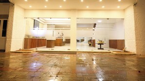 A hotel entrance with a glass facade, a reception desk, and a wet pavement.