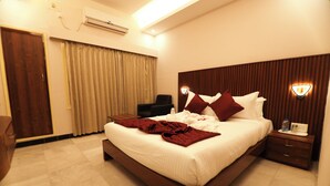 A neatly made bed with a white comforter and red throw pillows, a wooden headboard, a bedside table with a lamp, and a chair in a hotel room.