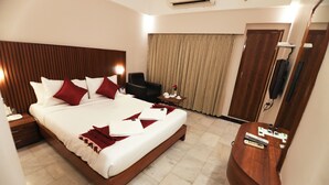 A hotel room with a large bed, a wooden headboard, a desk with a chair, a TV, and a curtain.