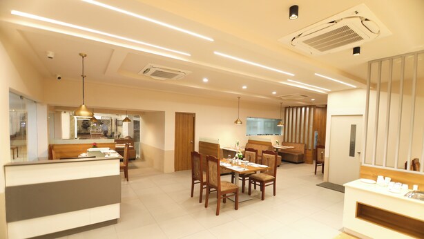 A modern hotel dining area with a reception desk, wooden chairs, and a long dining table.