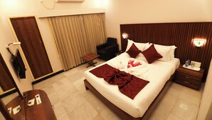 A hotel room with a bed, bedside table, nightstand, and a chair.