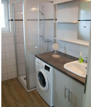 Ein kleines Badezimmer mit Waschmaschine, Waschbecken und einer Duschkabine.