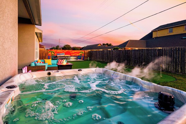 Un jardin avec un jacuzzi, une fresque murale colorée et une clôture en bois.
