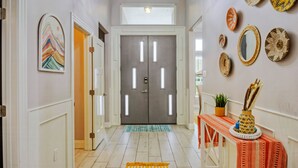 Un couloir doté d’une double porte, d’un tapis à motifs et de décorations murales comprenant des paniers tressés et un tableau.