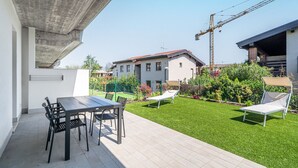 A patio with a table and chairs, a lawn with a lounge chair, and a building in the background.