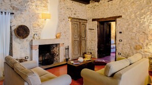 A stone-walled room with a fireplace, two sofas, and a wooden door.