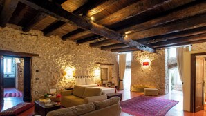 A rustic room with exposed wooden beams, stone walls, a sofa, a bed, and a red carpet.