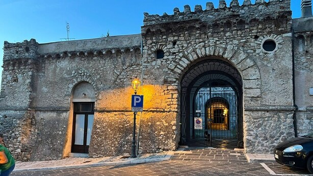 A historic stone building with a large arched entrance, a parking sign, and a paved street.