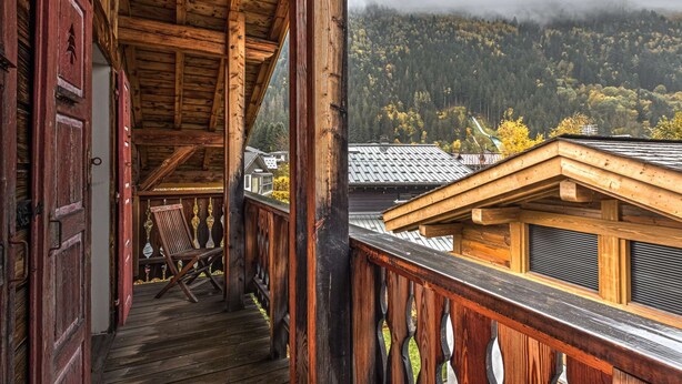 Eine Holzhütte mit Balkon, der auf ein bewaldetes Tal blickt.