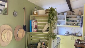 Eine gemütliche Küche mit grüner Wand, einem Holzhocker, einem Tisch mit Büchern und einem Regal mit Küchenutensilien.
