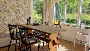 Ein Essbereich mit Holztisch, Stühlen und Blick auf Grün durch große Fenster.