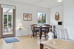 Een eetgedeelte met een tafel, stoelen, een lamp, een schilderij en uitzicht door een raam.