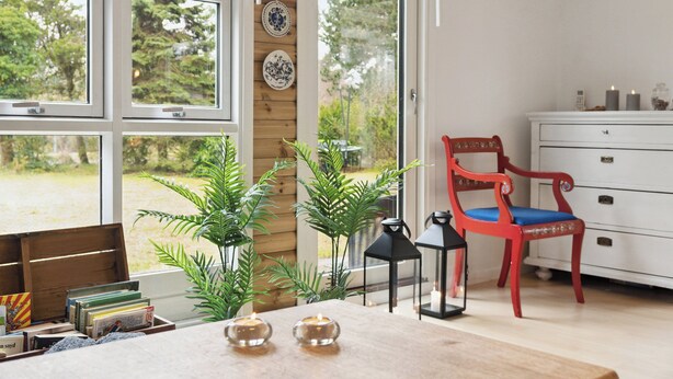 A room with large windows, a red chair, a white dresser, and various plants.