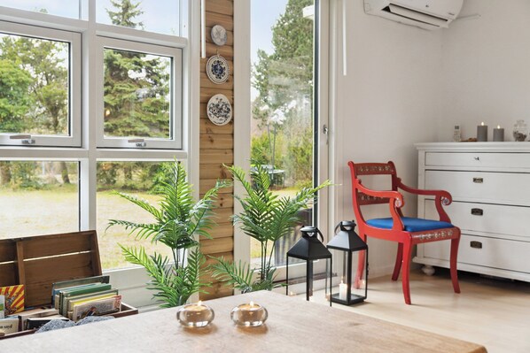 A room with large windows, a red chair, a white dresser, and various plants.