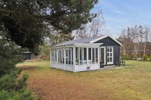 Een klein huis met een overdekte veranda, een omheinde tuin en een grote boom.