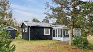A black wooden cabin with a covered porch, surrounded by trees and a grassy yard.