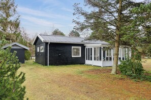 A black wooden cabin with a covered porch, surrounded by trees and a grassy yard.