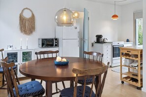 A modern kitchen with a round wooden table, chairs, a microwave, refrigerator, and a wooden shelf.