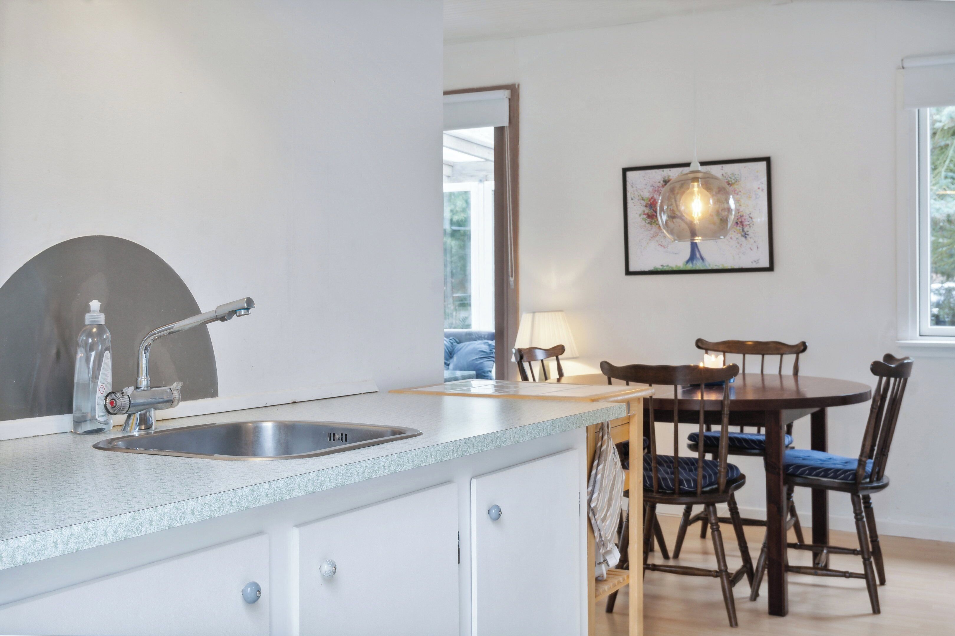 Een keuken met een spoelbak, een eettafel met stoelen en een hanglamp.