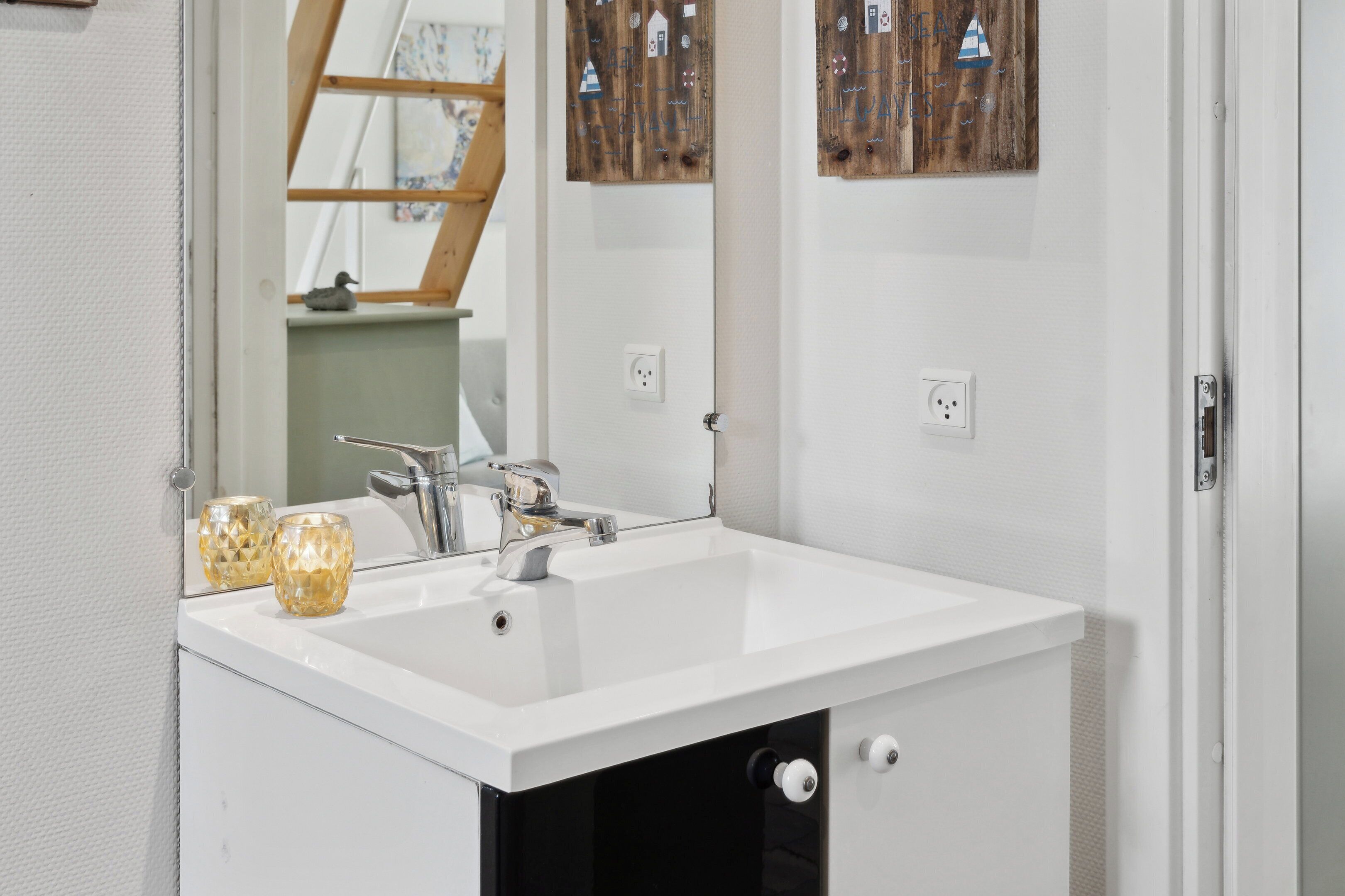 Een badkamer met een witte wastafel, een spiegel en houten decoraties aan de muur.