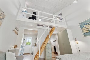 Un dormitorio tipo loft con escalera de madera, cama en zona superior, escritorio y vista a la cocina.