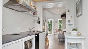 Een moderne keuken met witte kastjes, een ingebouwde oven en een aanrecht. Er is een eethoek met een tafel en stoelen zichtbaar op de achtergrond.