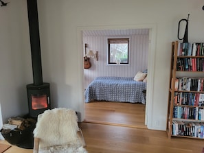 Une pièce chaleureuse avec un poêle à bois, une bibliothèque, un lit avec une literie à motifs et une fenêtre avec des stores.