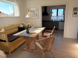 Een eetgedeelte met een houten tafel, een bank en rieten stoelen. Op de tafel staat een vaas met bloemen.