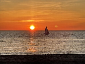 Een zonsondergang boven de oceaan met een zeilboot.