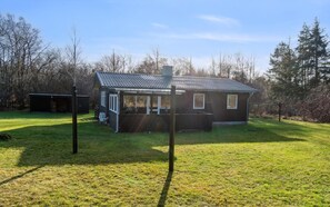 A single-story wooden house with a covered porch, a fenced yard, and a clear sky.