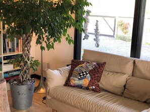 Ein Zimmer mit einer Couch, einer Zimmerpflanze, einem BĂŒcherregal und einem Fenster mit Aussicht.