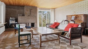 Una sala de estar acogedora con techo de madera, paredes de ladrillo, un sofá con cojines rojos, una mesa de centro y una chimenea.