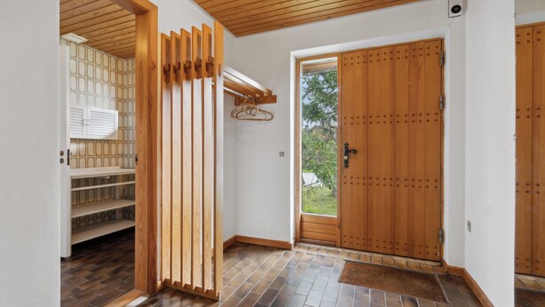 Un pasillo con puerta de madera, una estantería de madera y suelo de baldosas.