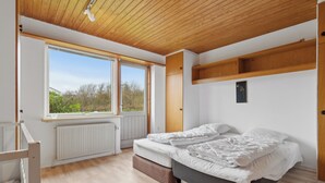 Un dormitorio con un ventanal grande, una cama, un radiador y techo de madera.