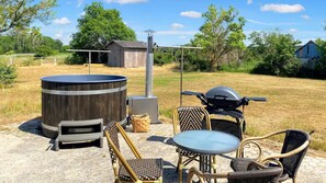 An outdoor patio with a hot tub, a grill, and wicker furniture.
